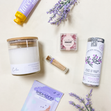 Flat lay of the Calm self-care gift box products, including a candle, lavender hand cream, herbal tea, moisturizing socks, matches, and boxed truffles.