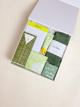 Open box containing green bath products on a beige background