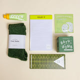 Collection of green-themed products including socks, a notepad, and bath products on a beige background