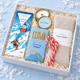 Angled view of the Après winter gift box filled with hot chocolate, cozy socks and festive treats