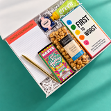 Game Night gift box with colorful snacks, First to Worst party game, Chaos Coordinator notepad, gold pen and Warm Wishes card.
