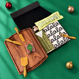 Holiday charcuterie gift box with serving board, gold cheese tools, festive snacks and a black-and-white falala cloth.