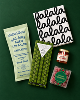 Small corporate holiday gift box with sweet and savory snacks arranged on a dark green background.