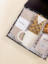 Close-up of Warm + Cozy gift box highlighting cream socks and cable-knit mug, ideal for fall gifting.