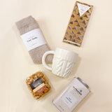 Lifestyle photo of Warm + Cozy fall gift box styled with candles and a blanket, a seasonal holiday gift idea.