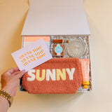 Flat lay of Summer Fun gift box items including peach bellini candy, teddy pouch, and champagne lotion