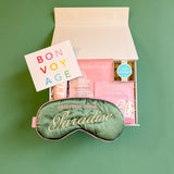 Flat lay of travel self-care gift box with getaway eye mask and skincare treats
