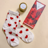 Valentine’s Day mini gift box for her with heart print socks, 2oz Be Mine soy candle, and Compartés red wine chocolate.”