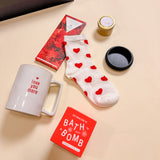 Be Mine Valentine’s luxury care package gift box including heart socks, soy candle, bath bomb, ring tray, red wine chocolate, and love you more mug.