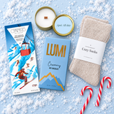 Après gift box products styled on a snowy light-blue background with cozy socks, chocolate and candy canes

