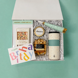 Birthday gift box for a friend featuring a speckled tumbler, birthday cake chocolate, caramel popcorn and a celebration candle.
