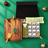 Christmas host gift box with a walnut charcuterie board, gold utensils and gourmet sweet and savory snacks.

