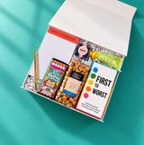 Angled view of Confete Game Night gift box filled with a party game, snacks, chocolate, candy, hand cream, notepad and gold pen.