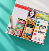 Close-up of Game Night gift box featuring First to Worst, caramel popcorn, colorful chocolate bar, candy, green tea hand cream and Chaos Coordinator notepad.