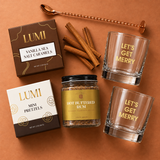 Holiday cocktail gift featuring two rocks glasses, a copper bar spoon, cinnamon sticks and sweet-and-salty snacks
