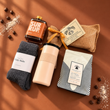 Flat lay of Slow Mornings gift box contents with coffee, Old Fashioned Pancake Mix, syrup, cozy socks and a travel tumbler.