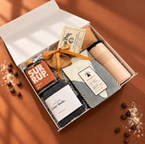 Open Slow Mornings gift box featuring pancake mix, cinnamon bun syrup, a beige tumbler and brown socks.