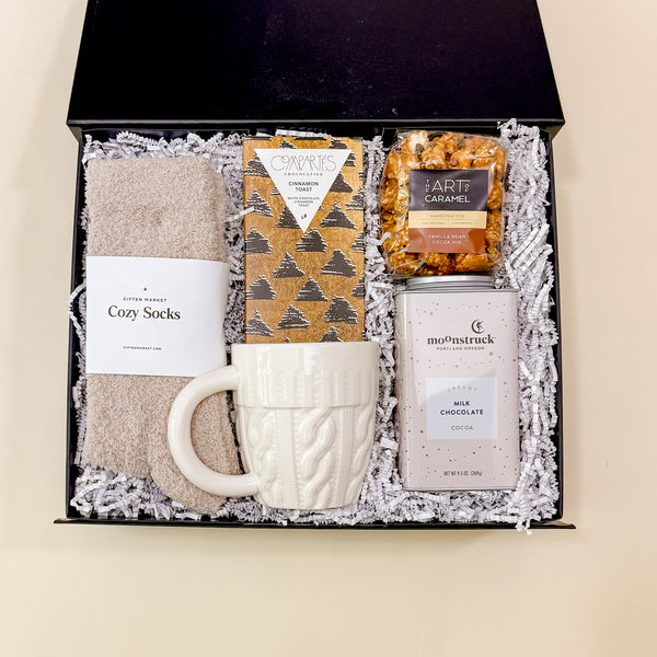 Warm + Cozy fall gift box viewed from above with socks, hot chocolate, caramel popcorn, and chocolate bar.
