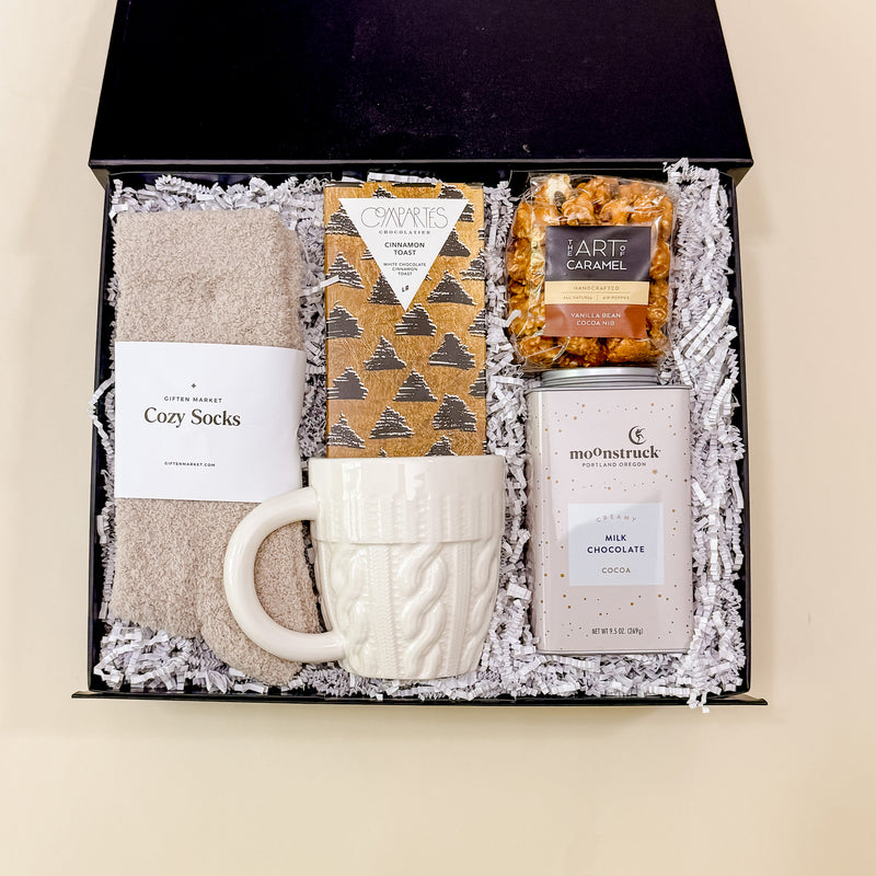 Warm + Cozy fall gift box viewed from above with socks, hot chocolate, caramel popcorn, and chocolate bar.
