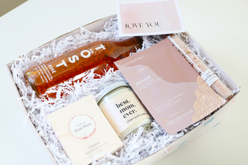 White backdrop with Rose Spa inspired mother's day gift items including Rose Wiine Gummies, Rose Sandlewood Bath Salt, Rose Tost sparkling beverage, Patchology Detox mud mask, and Best Mom ever candle
